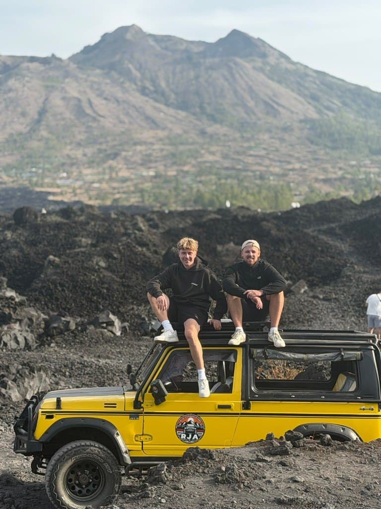 Two guests on the roof of a yellow jeep on the black lava field below Mount Batur