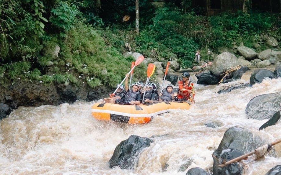 A raft crew cheering with paddles raised as they ride a rapid on the Ayung River