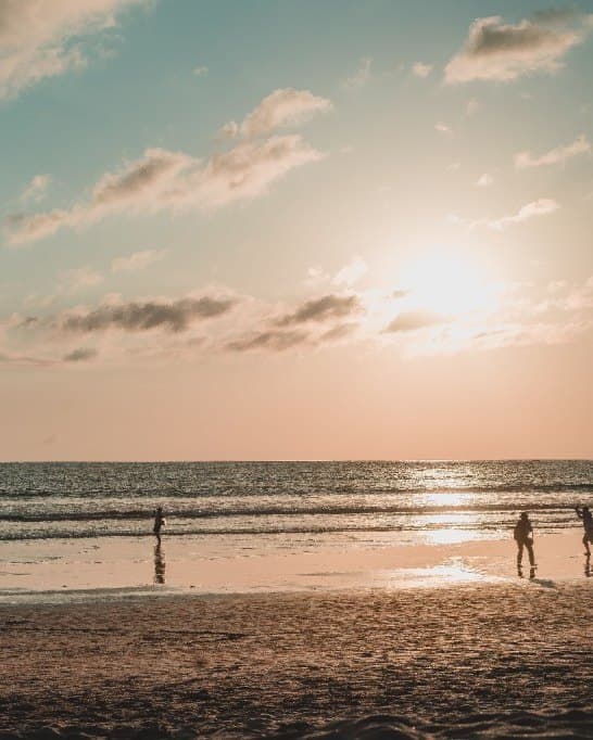 The sun setting over the water in Seminyak, people walking at the edge of the sea