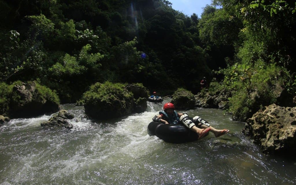A guest floating on a tube through a rocky jungle canyon, another tuber behind