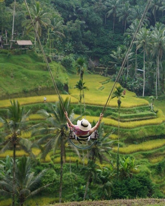 A guest in a sun hat on a jungle swing above the Tegallalang rice terraces near Ubud